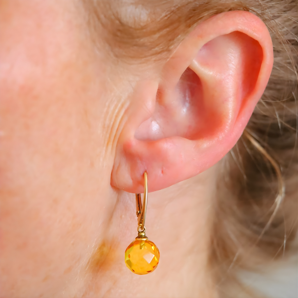 Close-up of an ear wearing a gold amber earring with a yellow gemstone.