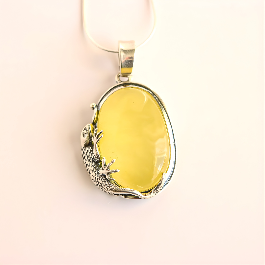 Yellow stone amber necklace with silver gecko design on a light pink background