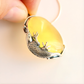 amber necklace with a yellow stone and silver lizard design held by a hand.
