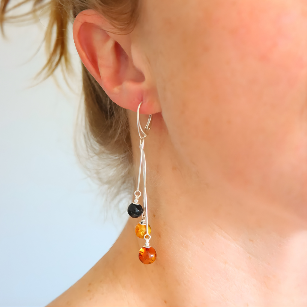 Close-up of an ear wearing a silver amber earring with beads against a light background