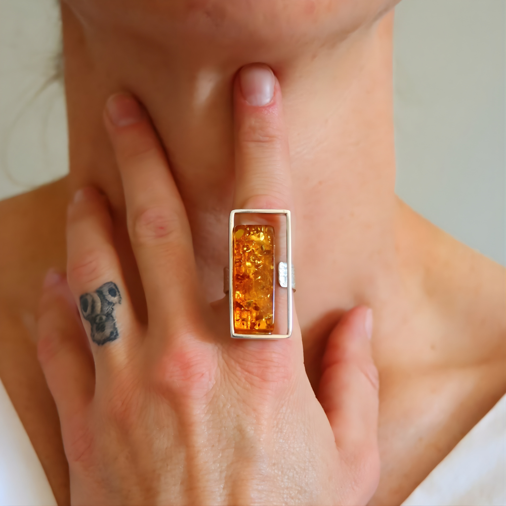 Close-up of a hand wearing a amber ring with a rectangular amber stone, held against a neutral background.