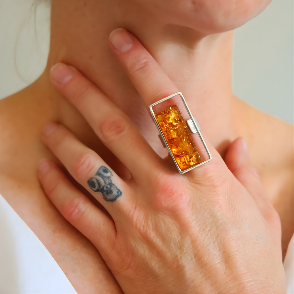 Close-up of a hand wearing a amber ring with amber stone on a neutral background