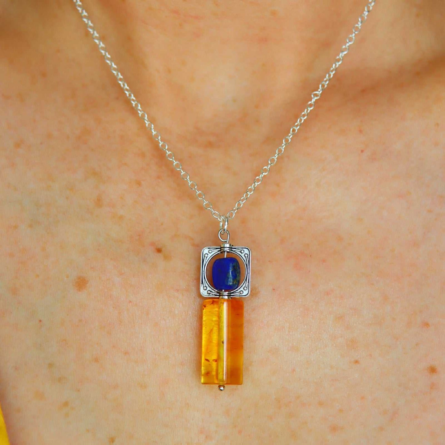 Close-up of natural Baltic lemon amber and deep purple lapis lazuli pendant in silver-plated pewter frame, handcrafted by artisan Alexis Cintron.