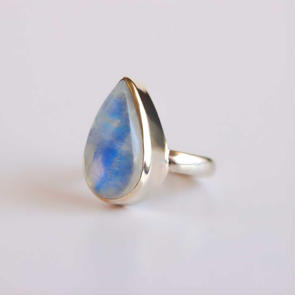 Silver moonstone ring with a teardrop-shaped rainbow moonstone on a light gray background