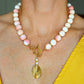 Close-up of a handmade Queen Conch and gold beaded statement necklace with pink and white beads, freshwater pearls, and a front gold toggle clasp with a hammered gold pendant.
