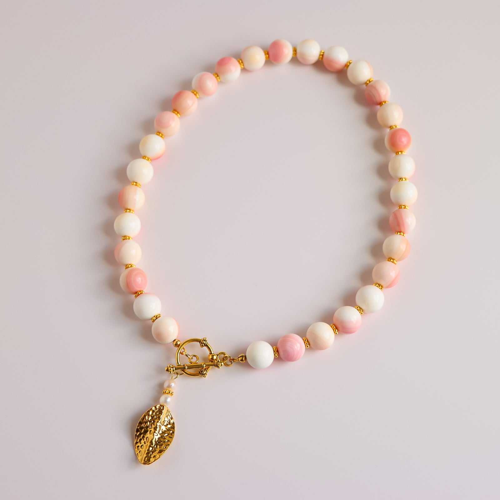 Handmade Queen Conch and gold beaded statement necklace with pink and white beads, freshwater pearls, and a gold drop pendant by Alexis Cintron
