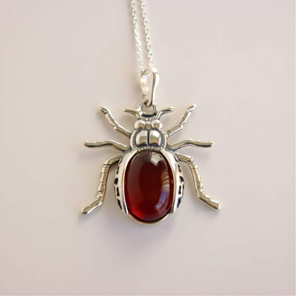 Silver scarab amber pendant shaped like a beetle with a red stone on a light gray background