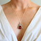 Silver scarab amber pendant with a red stone on a necklace, worn by a person in a white top.