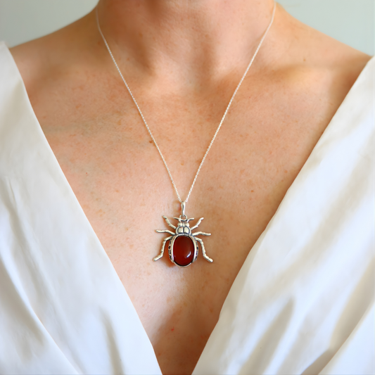 Silver scarab amber pendant with a red stone on a necklace, worn by a person in a white top.