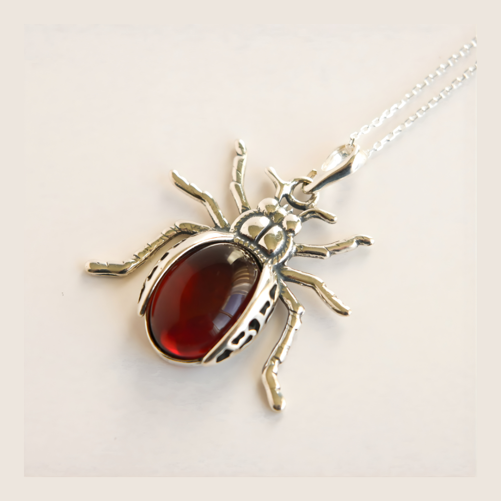 scarab shaped amber pendant with a red stone on a white background