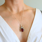 Necklace with a scarab amber pendant featuring a red stone worn by a person in a white top.