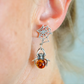 Silver spider and web amber earrings with amber bead on a person's ear.
