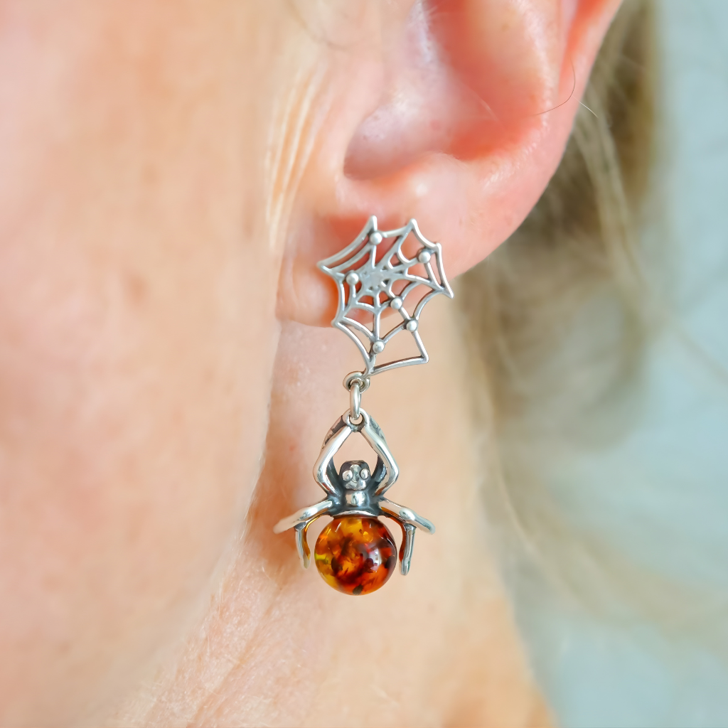 Silver spider and web amber earrings with amber bead on a person's ear.