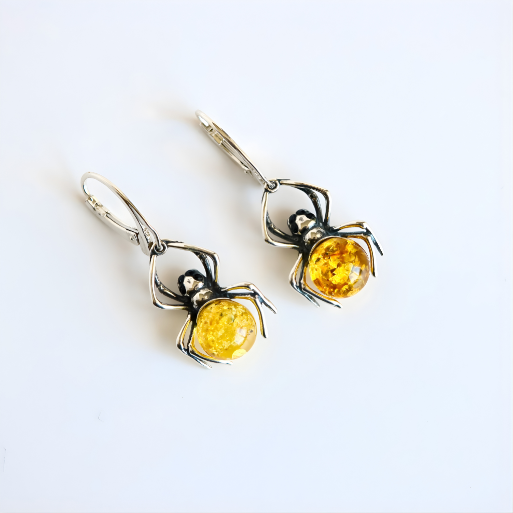 Spider-shaped amber earrings with yellow gemstones on a white background