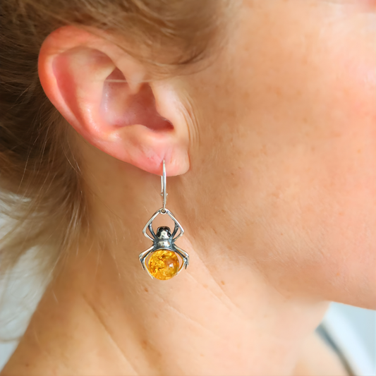 Close-up of a spider-shaped amber earring with a yellow gemstone worn by a person.
