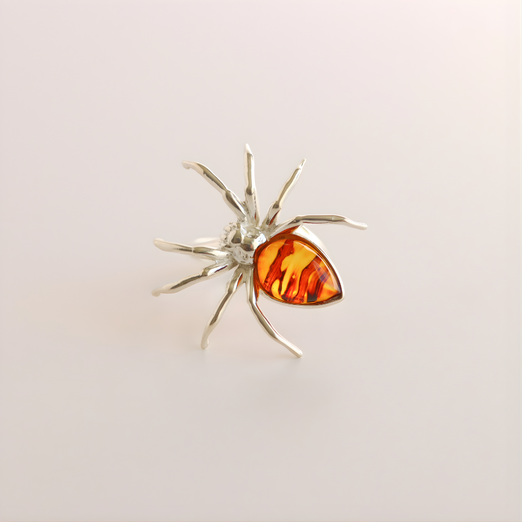 Silver spider-shaped statement ring with a red-orange gemstone on a light gray background