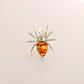 Silver spider-shaped statement ring with a amber-colored center on a light gray background