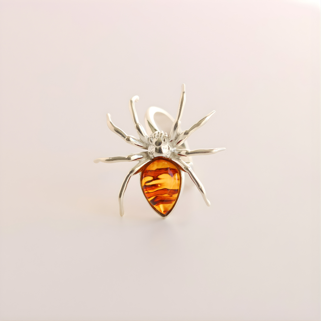 Silver spider-shaped statement ring with a amber-colored center on a light gray background