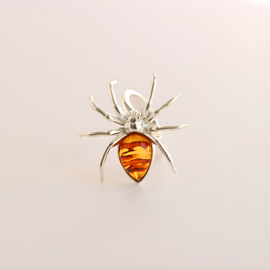 Silver spider-shaped statement ring with a amber-colored center on a light gray background