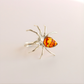 Silver spider-shaped statement ring with amber-colored gemstone on a light beige background