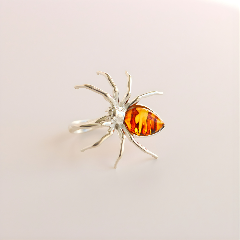 Silver spider-shaped statement ring with amber-colored gemstone on a light beige background