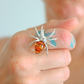 Silver spider-shaped statement ring with amber stone held between fingers
