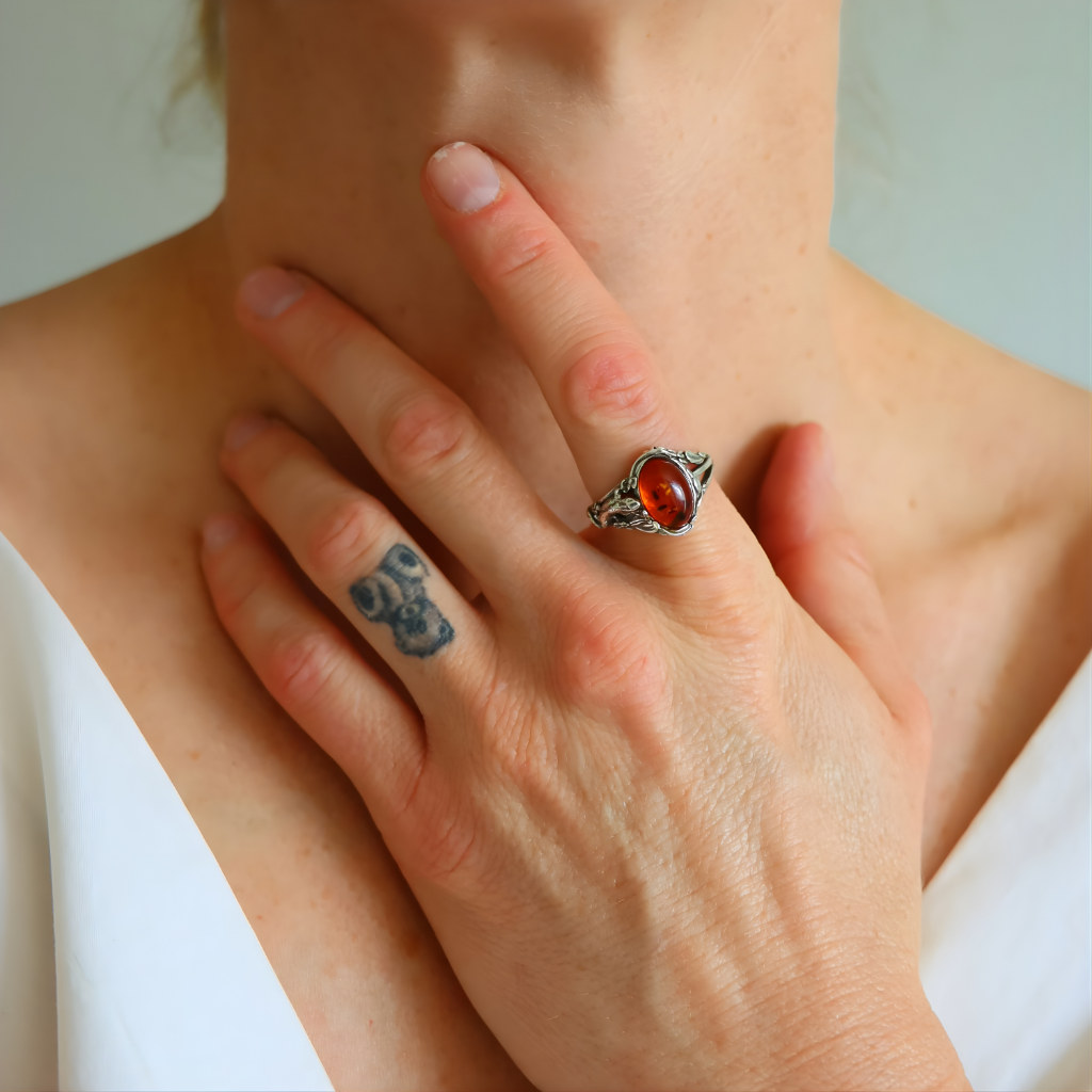 Close-up of a hand wearing a silver amber ring with a red stone, touching the chin.