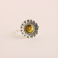 Silver green amber ring with a sunflower design and yellow gemstone on a light pink background