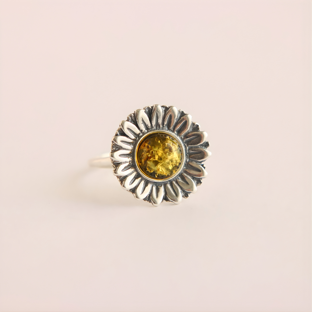 Silver green amber ring with a sunflower design and yellow gemstone on a light pink background