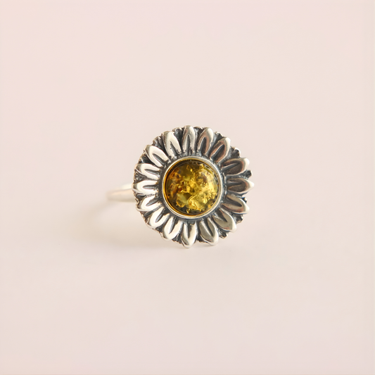 Silver green amber ring with a sunflower design and yellow gemstone on a light pink background