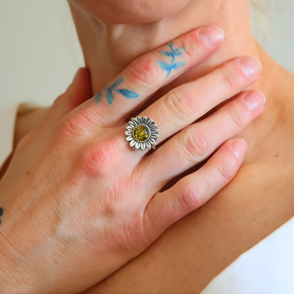 Hand wearing a silver green amber ring with a yellow stone and floral design on a light background