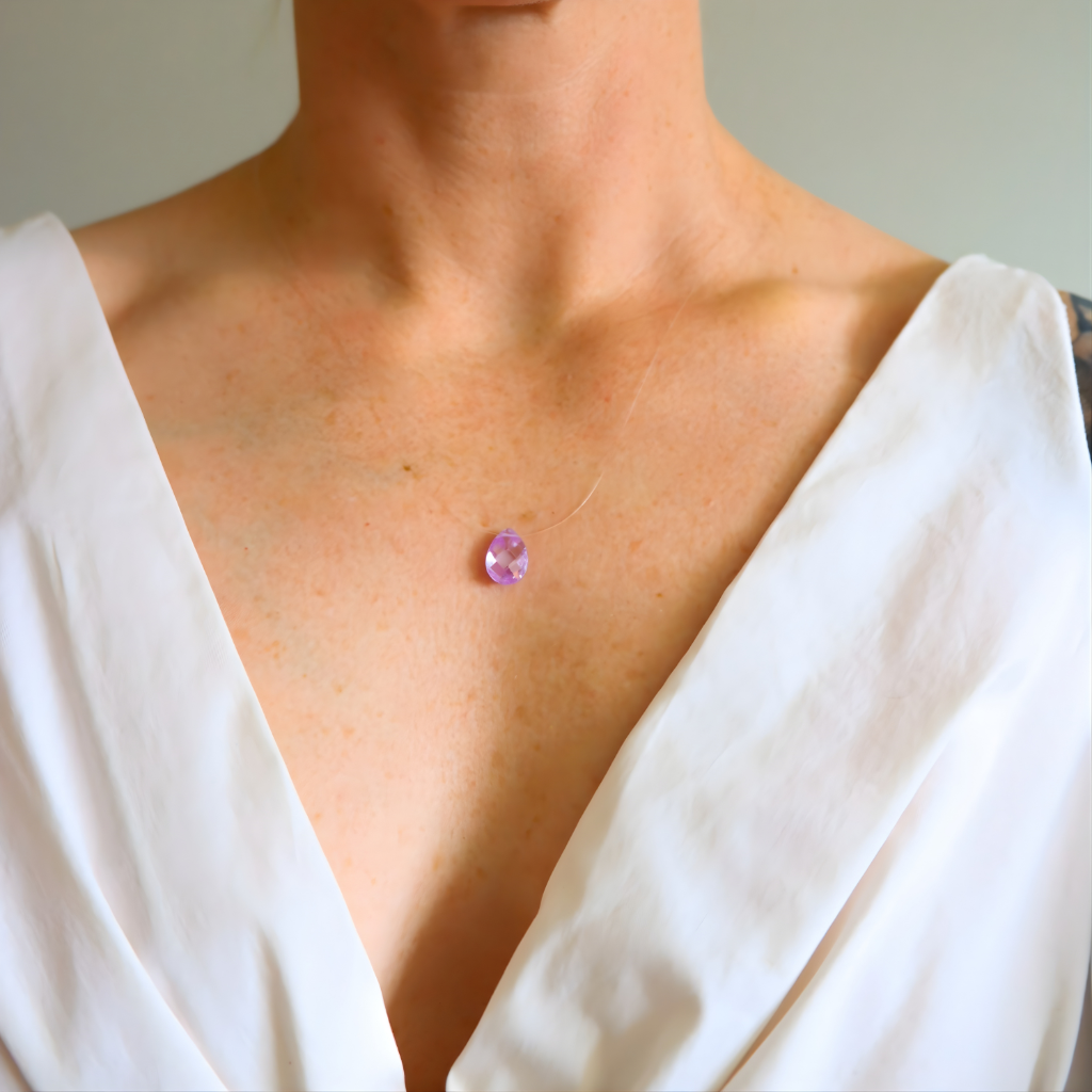 Close-up of a amethyst necklace with a pink gemstone on a person wearing a white top.