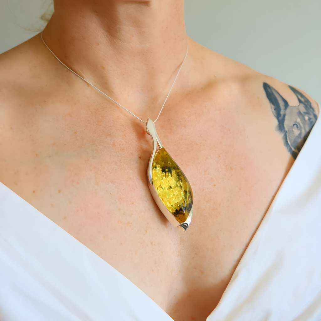 Person wearing a amber necklace with a pendant featuring yellow and green colors.