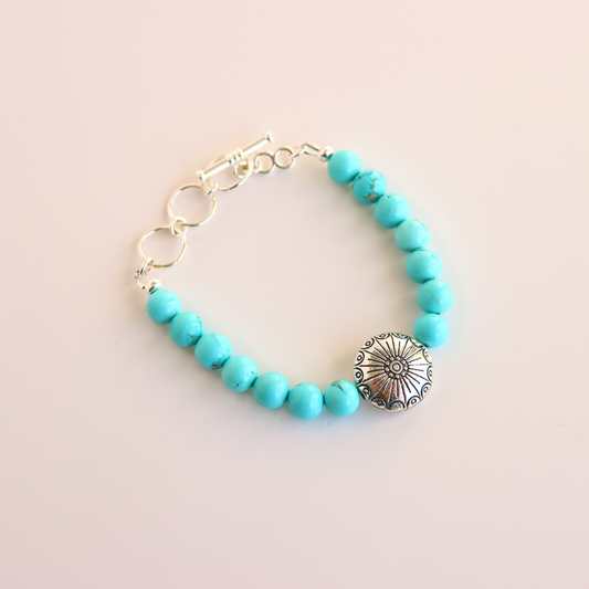 Turquoise beaded howlite bracelet with a silver sunflower charm on a light beige background