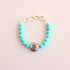 Turquoise beaded howlite bracelet with a silver charm on a light pink background