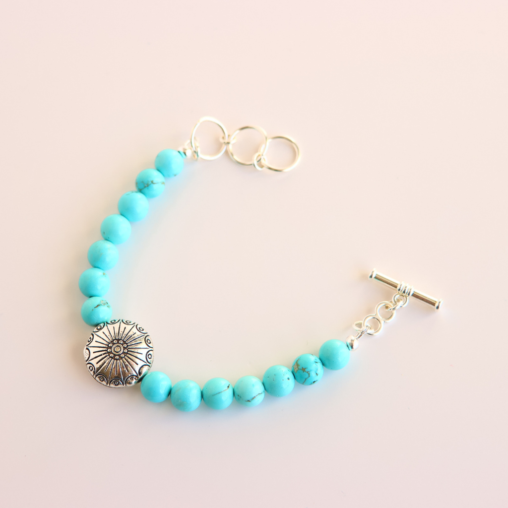 Turquoise beaded howlite bracelet with a silver clasp on a light pink background