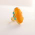 Gold amber ring with a large orange stone and smaller turquoise stones on a light background