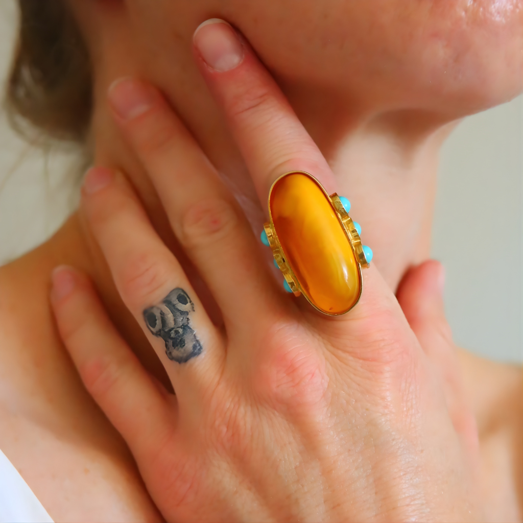 Close-up of a hand wearing a large yellow amber ring with turquoise stones, covering part of the face.