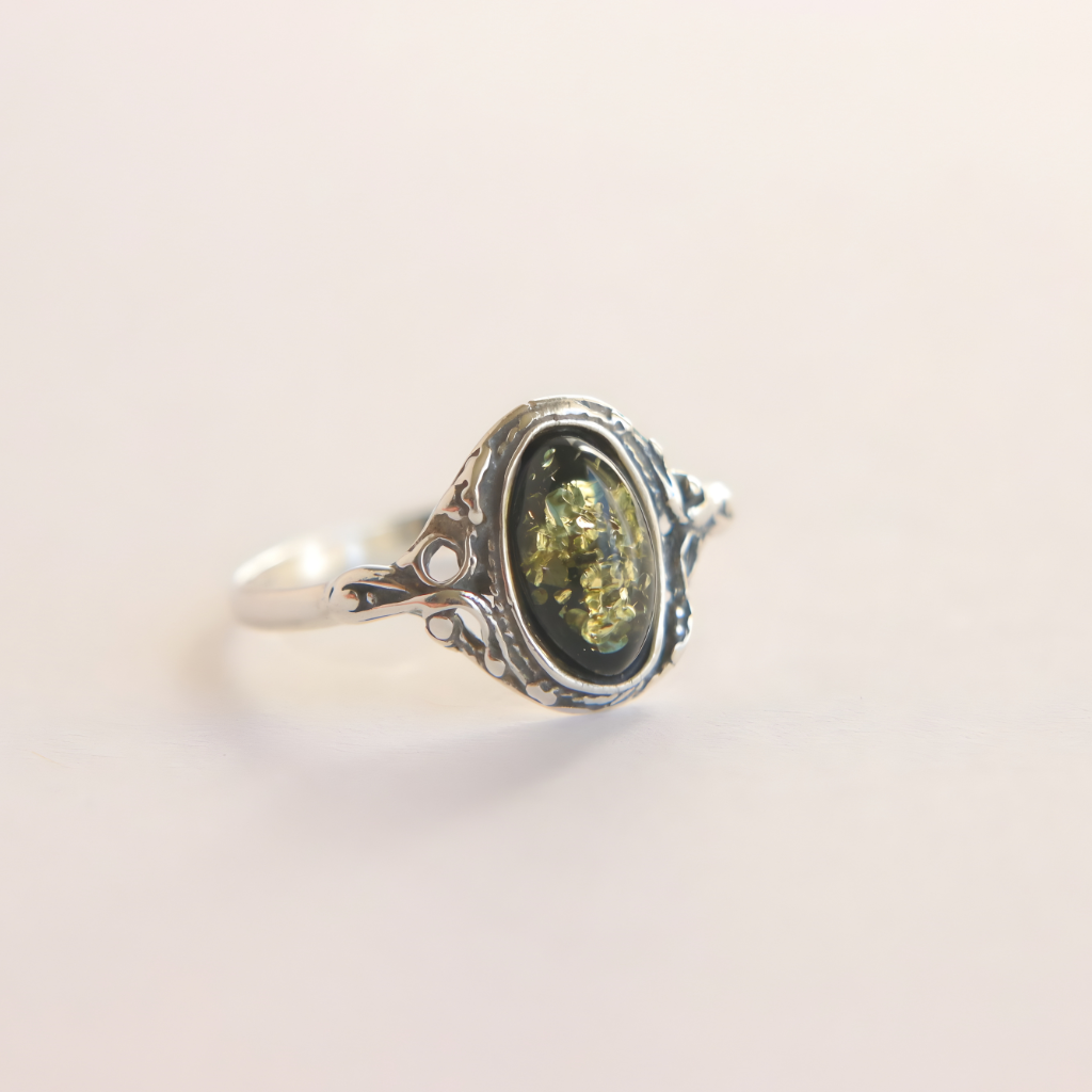 Silver amber ring with a green gemstone on a light beige background