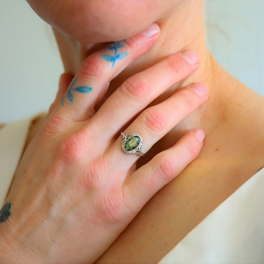 Close-up of a hand wearing a amber ring with a green gemstone, touching the wrist.