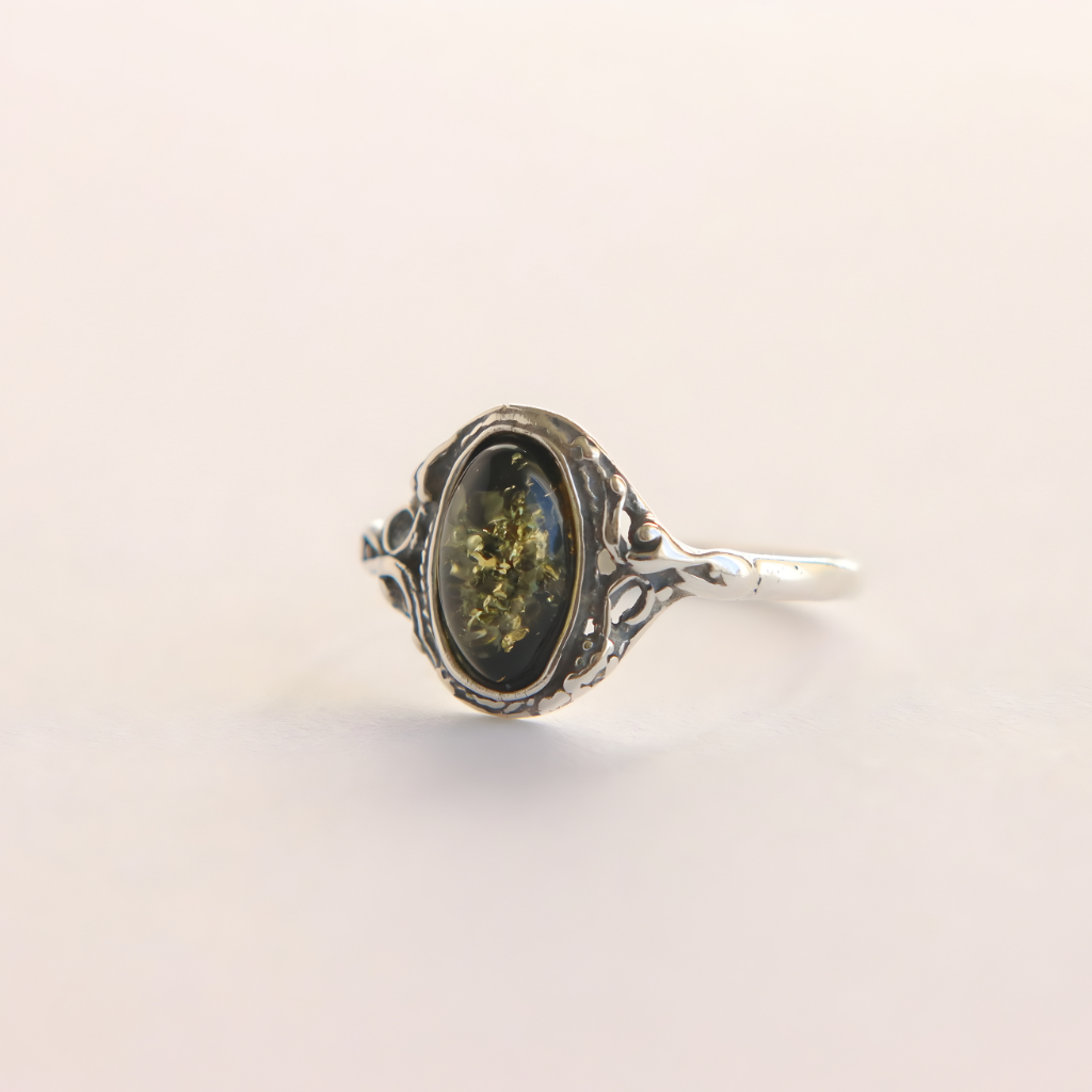 Silver amber ring with a green gemstone on a light beige background