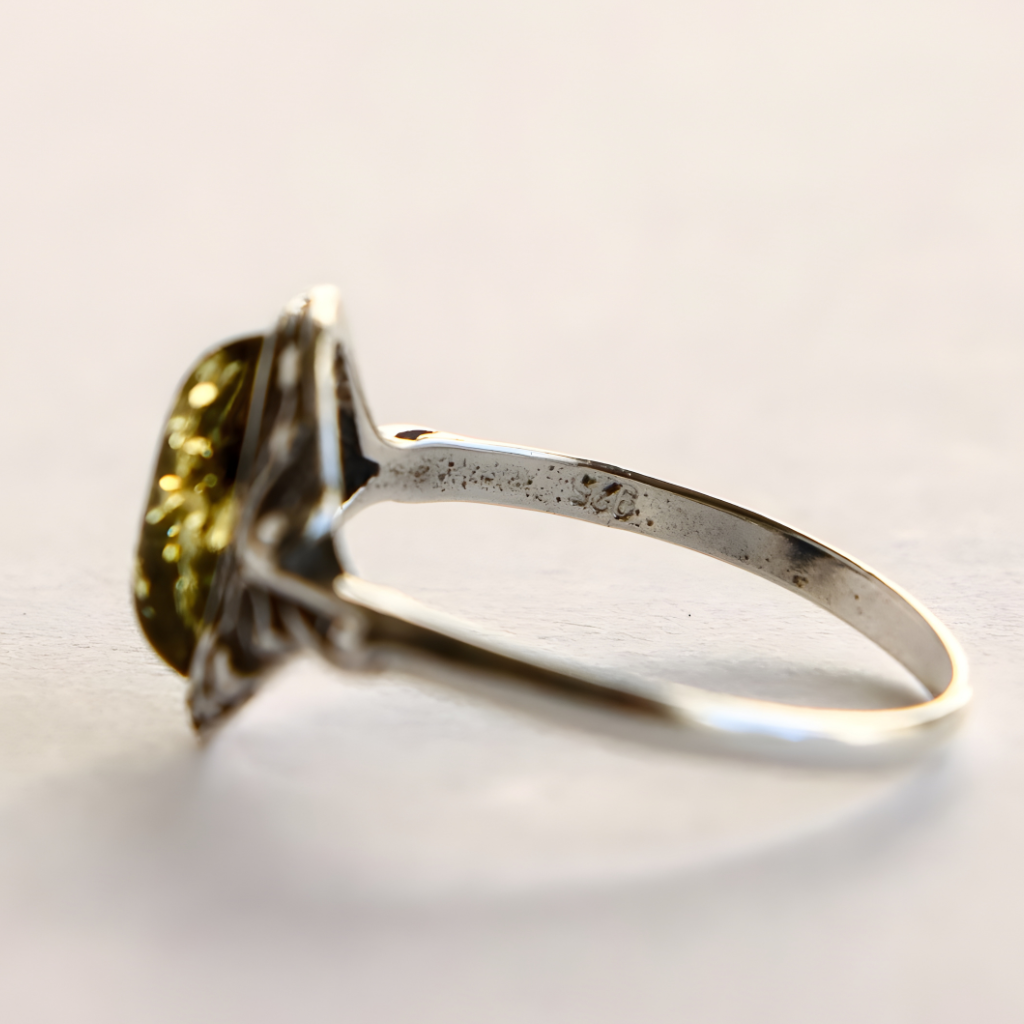 Silver amber ring with a green gemstone on a light background