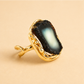 Gold amber ring with a large black stone on a beige background
