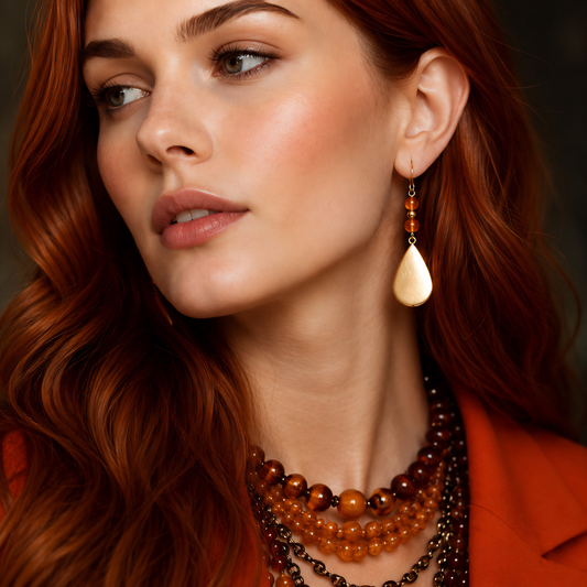 gold drop earrings with amber gemstone on model with red hair on black background