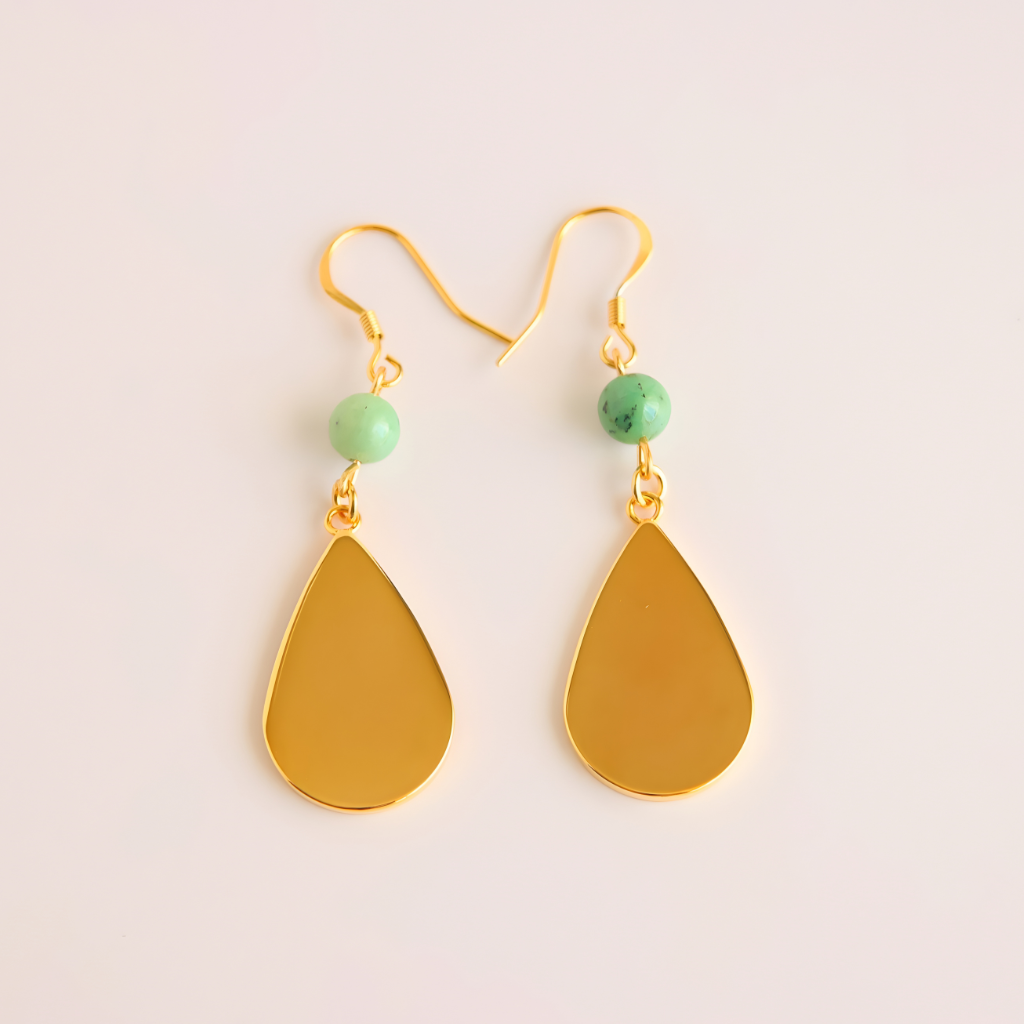 Gold drop earrings with green beads on a light beige background