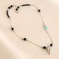 raven skull Necklace with black and blue beads and a skull pendant on a beige background