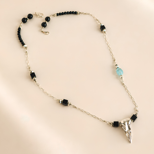 raven skull Necklace with black and blue beads and a skull pendant on a beige background